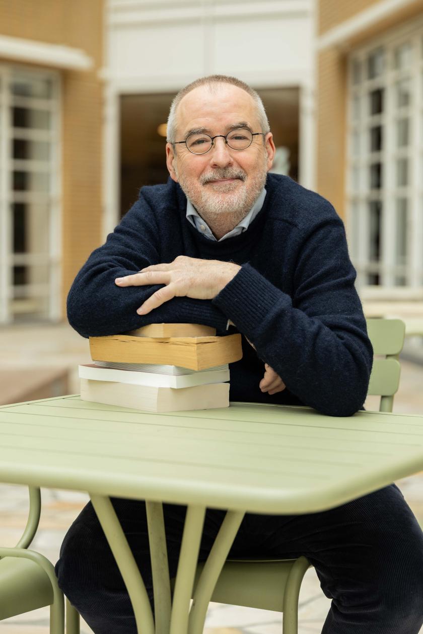 Man met bril glimlacht steunend op een stapel boeken