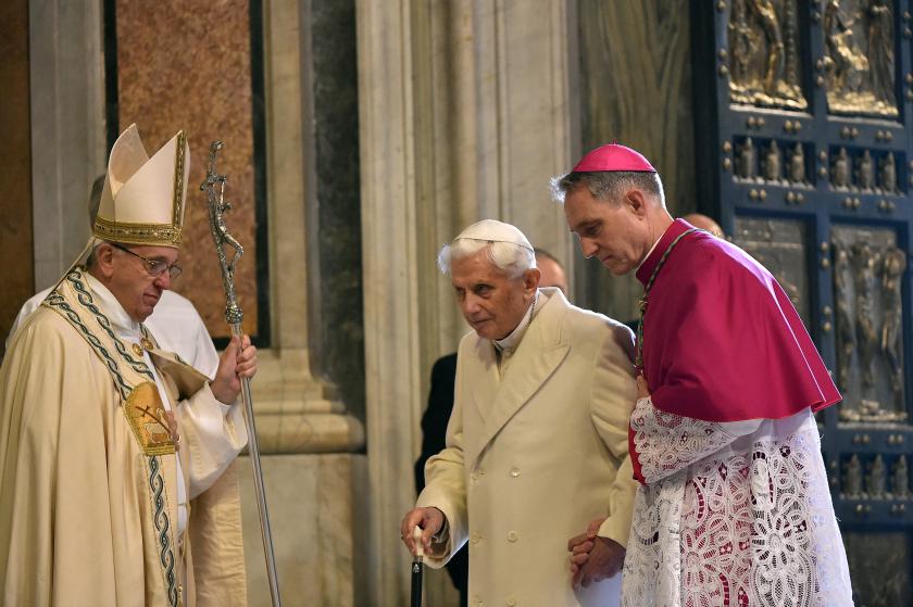 - [ ] Pope Emeritus Benedict XVI (C) is helped by the prefect of the papal household Georg Gaenswein (R) to pass the "Holy Door" as Pope Francis (L) looks on, during the ceremony marking the start of the Jubilee Year of Mercy, on December 8, 2015 in Vatican. AFP PHOTO / ALBERTO PIZZOLI 