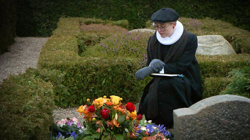 Pastor in Search of Paradise foto 2 Jonge vrouw zit aan een graf met onder bloemen