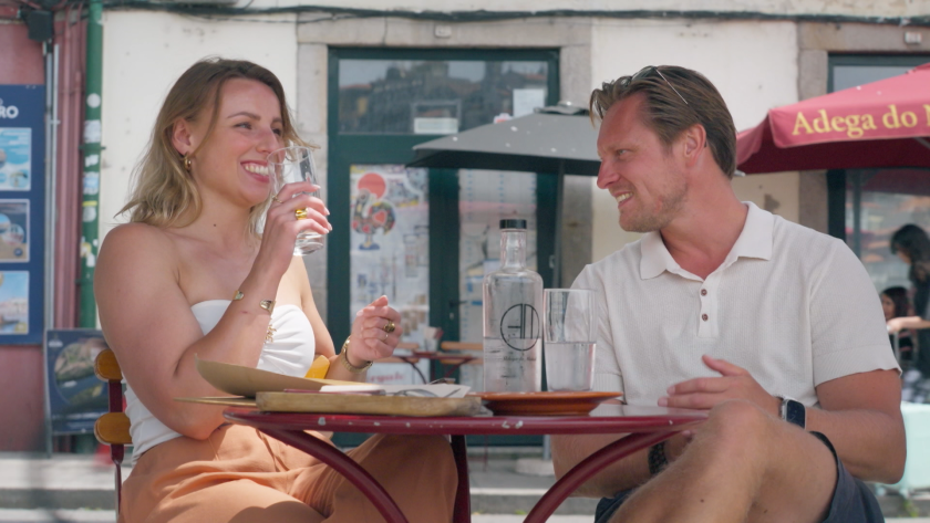Man en vrouw op terras lachend naar elkaar met drankje vast