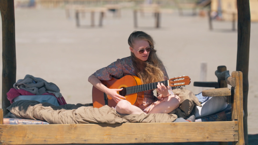 Vrouw met gitaar in kleermakerszit onder doek op strand