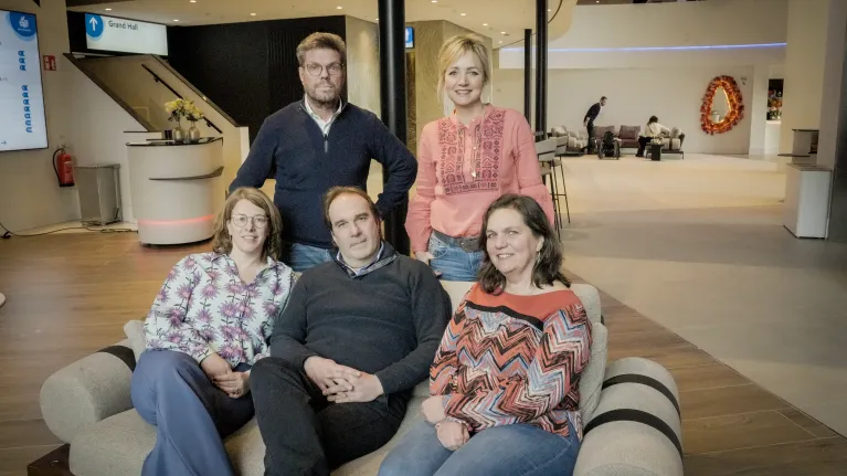 Drie mensen zitten op een bank en twee mensen staan erachter