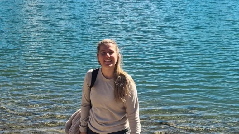 Vrouw staat met hond bij het water en kijkt lachend de camera in