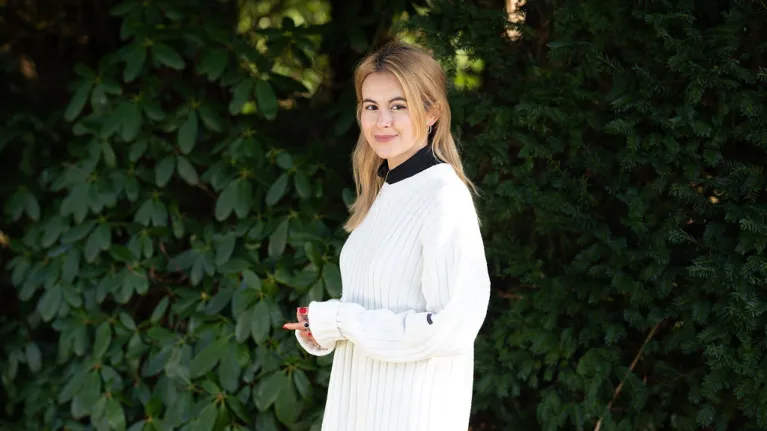 Blonde jonge vrouw met witte trui voor een grote struik