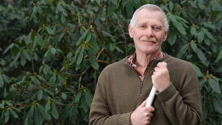 Een volwassen man houdt een schoffel vast 