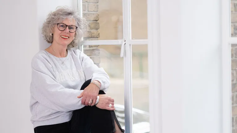 Volwassen vrouw met grijze trui zit in het raamkozijn