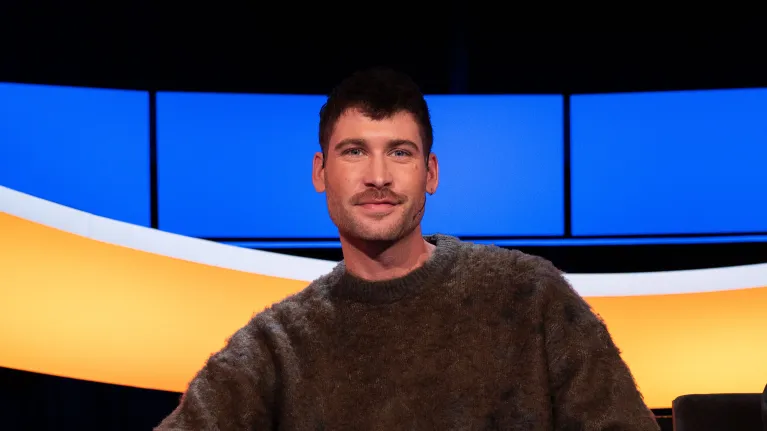 Man met bruin haar en snor en bruine trui