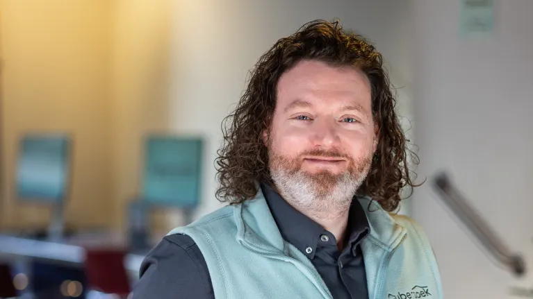 Man met lang haar staat met handen in zijn zakken en kijkt in de camera