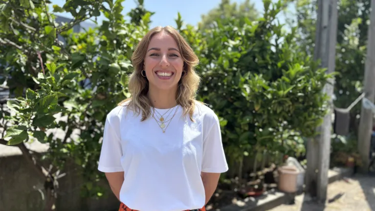 Vrouw in wit shirt voor een heg lachend naar camera