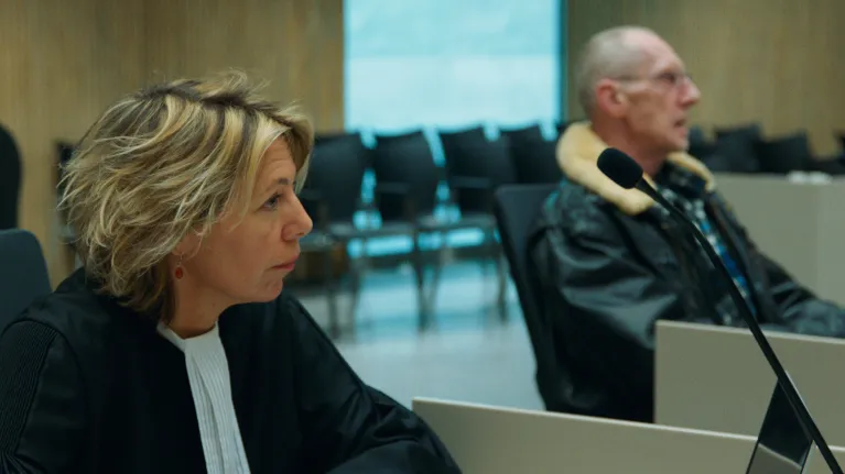 Een vrouw met kort blond haar in een rechters kledij naast een cliënt 