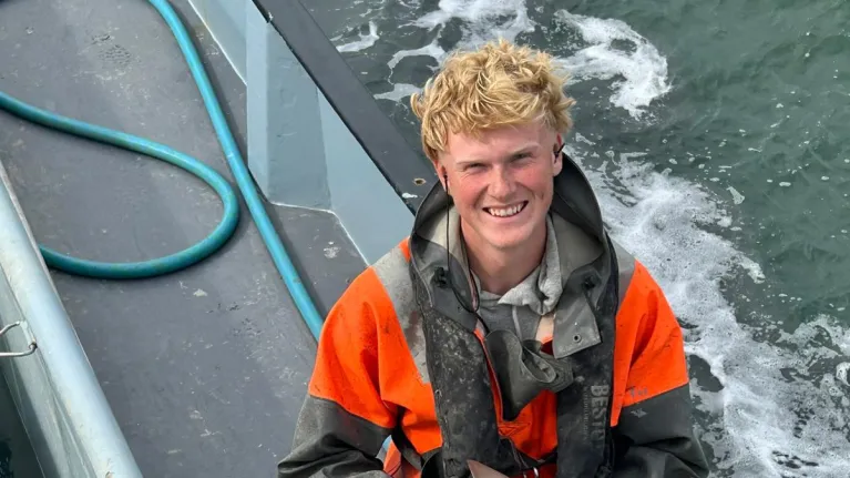 Een jongen staat op een boot met een kleine haai in zijn handen