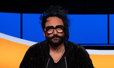 Man met zwart haar, baard en bril in studiostoel