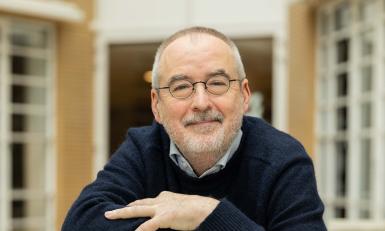 Man met bril glimlacht steunend op een stapel boeken