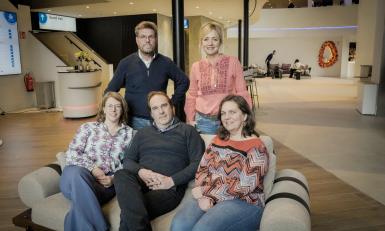 Drie mensen zitten op een bank en twee mensen staan erachter