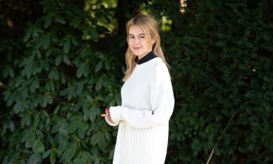 Blonde jonge vrouw met witte trui voor een grote struik