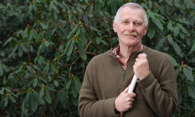 Een volwassen man houdt een schoffel vast 