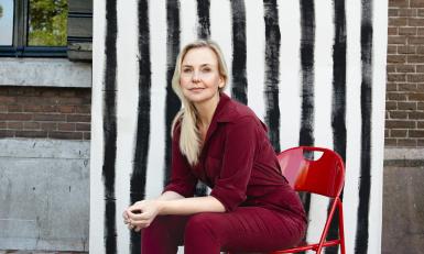 Blonde vrouw in rood pak zit voor zwart-wit-achtergrond