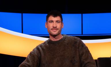 Man met bruin haar en snor en bruine trui