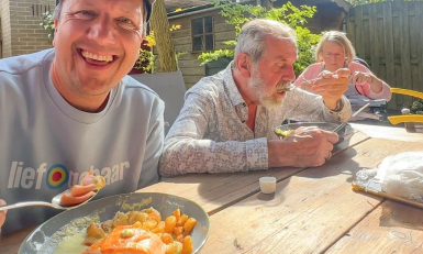 Lachende man met pet eet met oudere man en vrouw