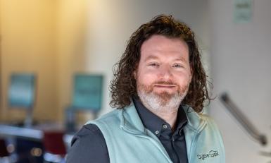 Man met lang haar staat met handen in zijn zakken en kijkt in de camera