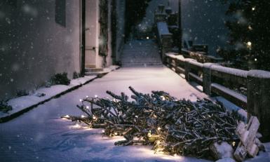 Een kerstboom met kerstlichtjes ligt buiten op de stoep in de sneeuw