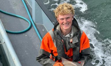 Een jongen staat op een boot met een kleine haai in zijn handen