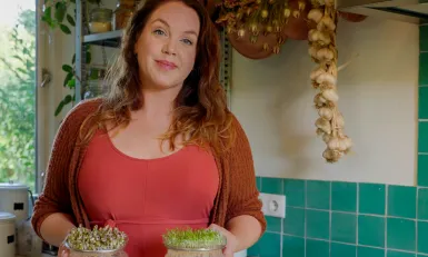 Een vrouw in rode kleding houdt twee schaaltjes met kiemgroente vast