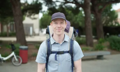 Man met pet en rugzak in blauwe blouse met korte mouwen