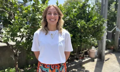 Vrouw in wit shirt voor een heg lachend naar camera