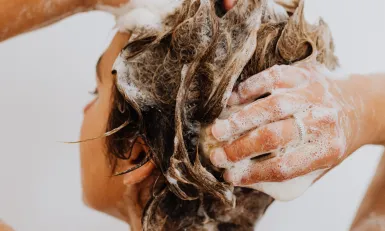 Een vrouw onder de douche die haar haren wast met shampoo