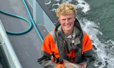 Een jongen staat op een boot met een kleine haai in zijn handen